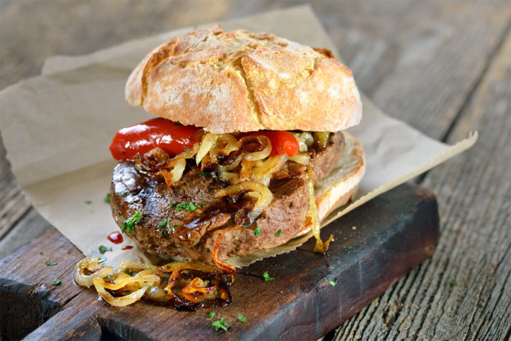 Steak im Brötchen mit gerösteten Zwiebeln und Paprika auf einem Holzbrett.