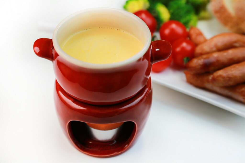 Ein kleines Käsefondue mit Wurst steht auf dem Tisch