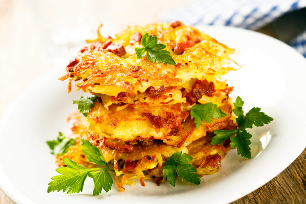 Kartoffelpuffer mit Speck auf einem weißen Teller gestapelt.