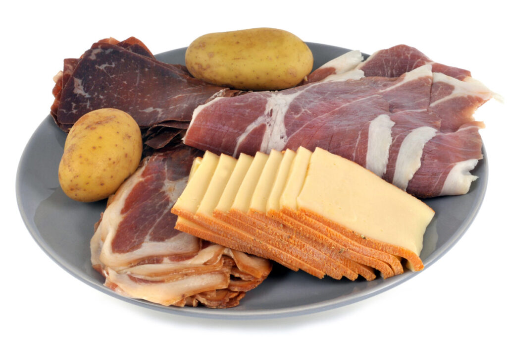 Ein teller gefüllt mit Käse, Schinken und Kartoffeln für ein Raclette.
