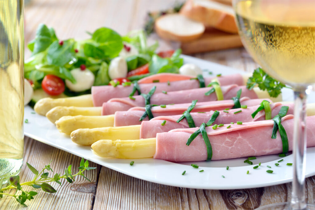 Spargel Schinkenröllchen auf einer weißen Platte mit Petersilie