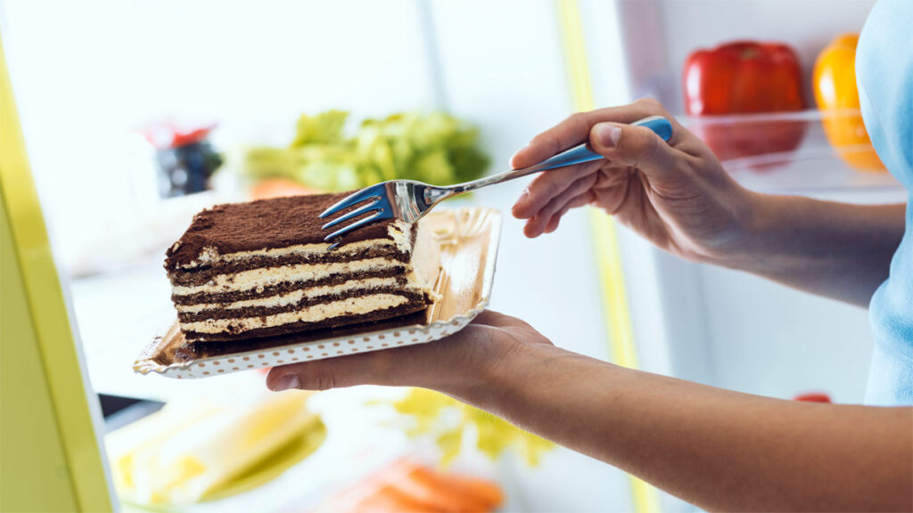Frau isst Sahnekuchen aus dem Kühlschrank