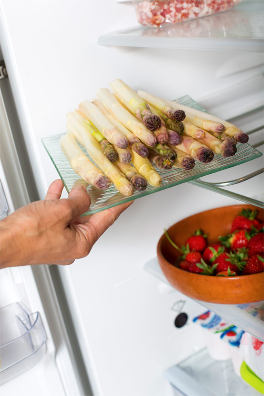 Frau holt weißen Spargel aus dem Kühlschrank