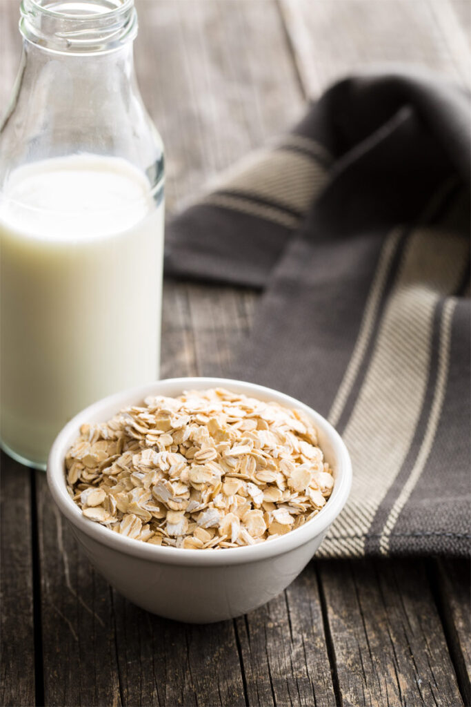 Haferflocken in einer Schüssel stehen neben einer Flasche Milch