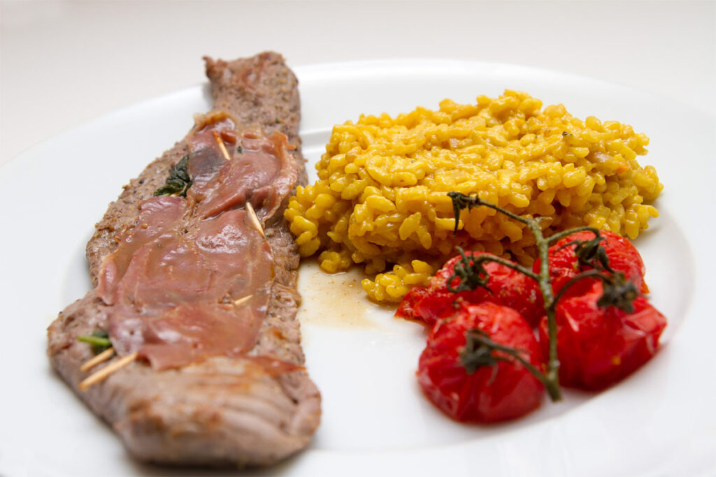 Teller mit Saltimbocca ala Romana mit Reis und gegrillten Tomaten