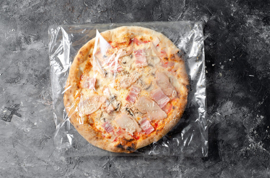 Tiefkühlpizza in Plastikfolie verpackt liegt auf dem Tisch.