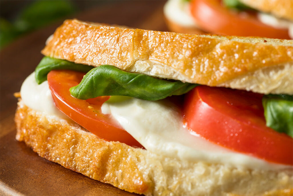 Ein Mozzarella Caprese Panini liegt auf einem Holzbrett.